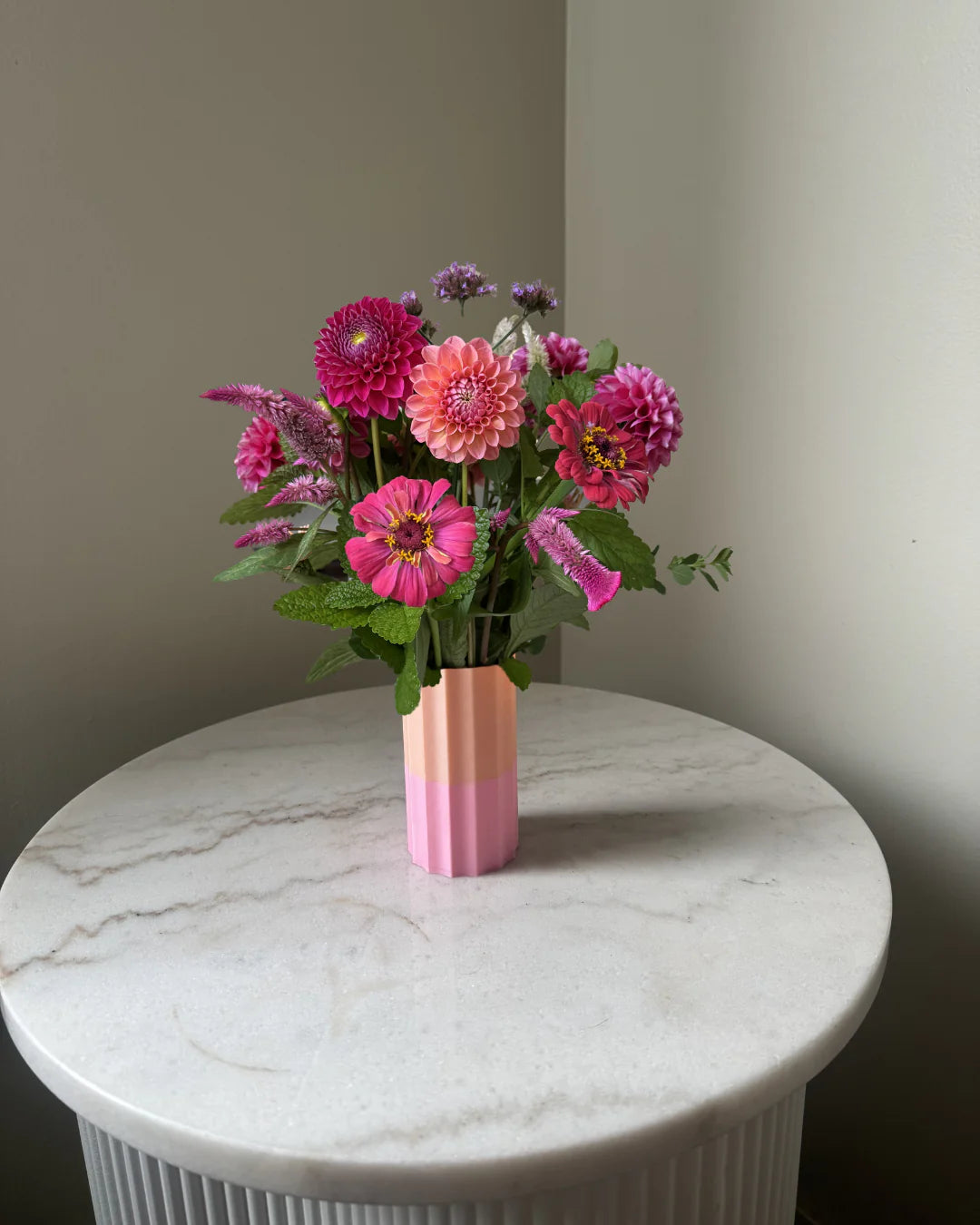 Bouquet of pink and purple flowers in a 2 toned pink and peach coloured vase on a marble table.