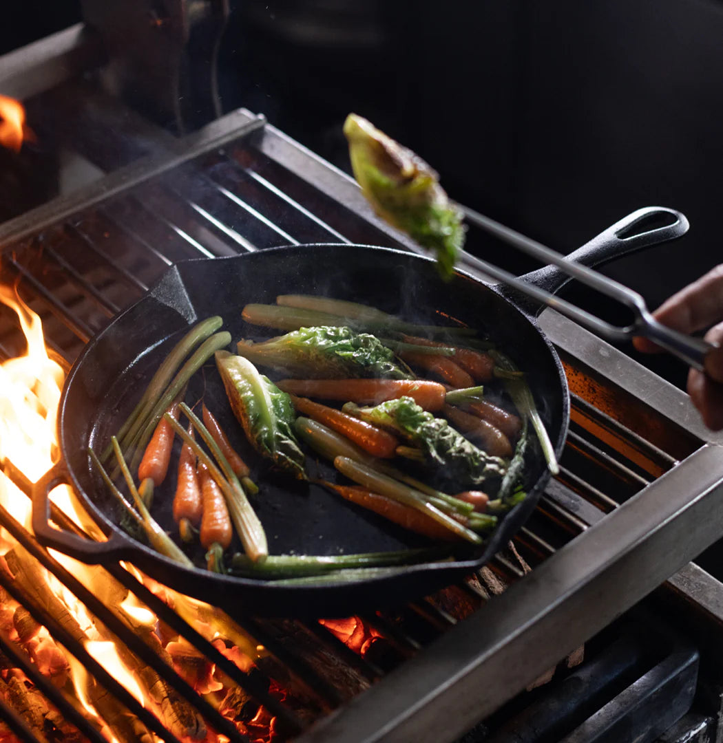 Vegetables being grilled in a cast iron skillet on a barbecue.